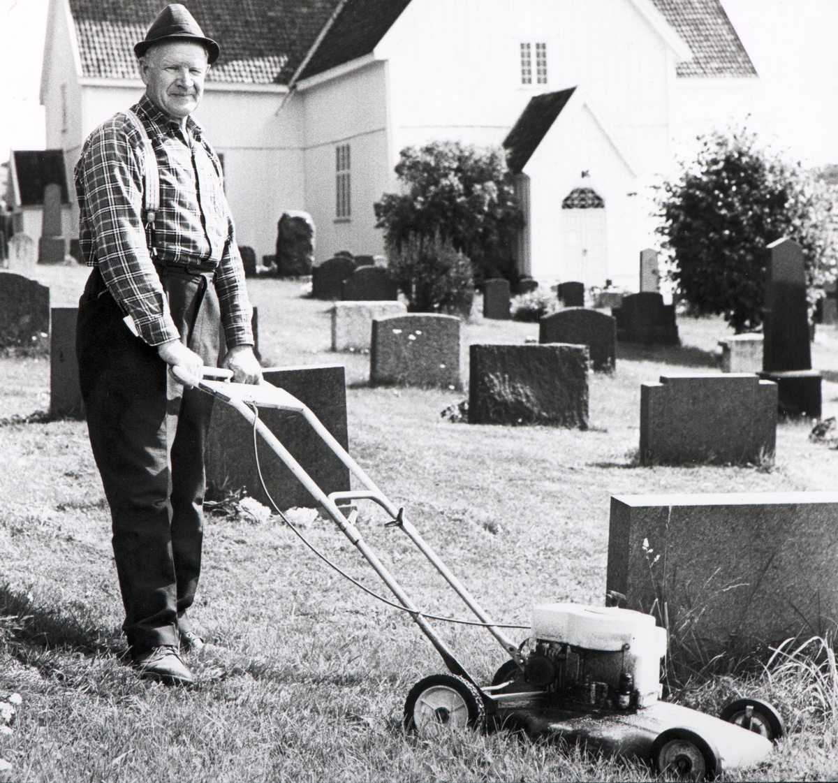 Veldre kirke, Kirketjener Gunnar Solli i over 40 år, klipper plenen på kirkegården, 1975. 