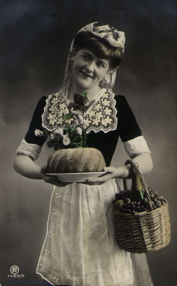 Postkort. Jule- og nyttårshilsen. Fotografisk motiv. Svart/hvitt. Pyntet kvinne med kakefat og fruktkurv. Stemplet desember 1909.