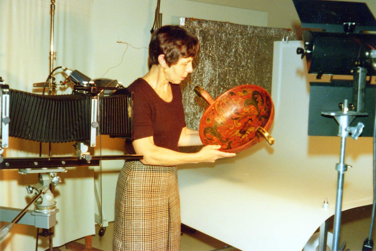 Bergljot Sinding fotograf på Norsk Folkemuseum, i sitt atelier i desember 1974, holdende en rosemalt trøys.