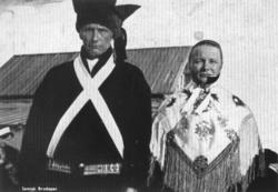 Nærbilde av samisk brudepar, et hus i bagrunnen. Karasjok.