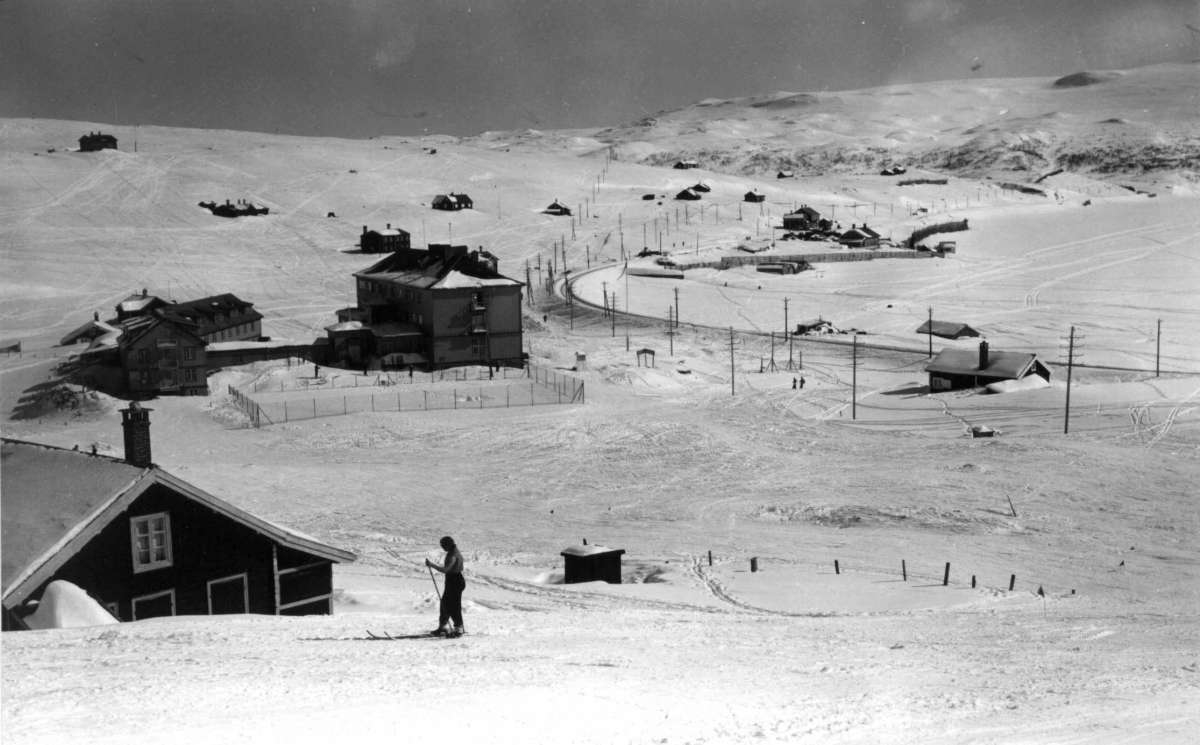 Ustaoset, Hallingdal. Vinterlandskap. Fjellområde med hyttebebyggelse. Skiløpere er ute i løypene. Til høyre ses jernbanespor.