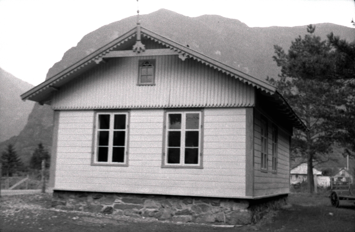 Rikheim, Lærdal, Sogn og Fjordane, bygget 1869. Lite hvitt skolehus med mørke kanter og fjell i bakgrunnen.. Registrering utført 1958-59 av Johan Schiong for Noregs Lærarlag. 