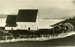 Trondenes kirke med inngjedet gravlund ved sjøen.