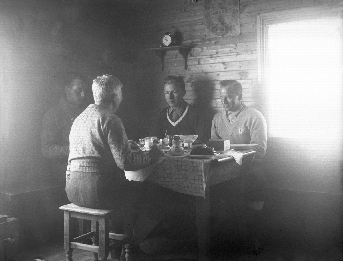 Flere menn sitter rundt et froksotbord. Fotografert påsken 1934.