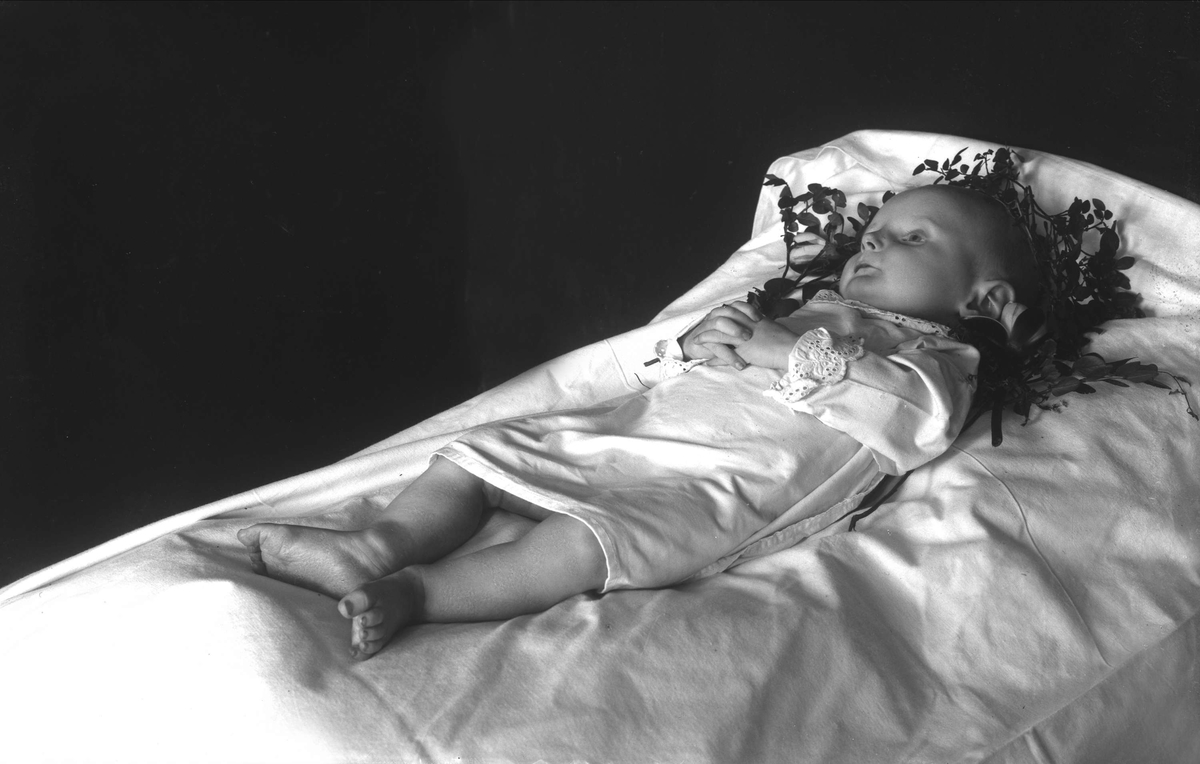 Post mortem-fotografi. 
Dødt barn i seng.