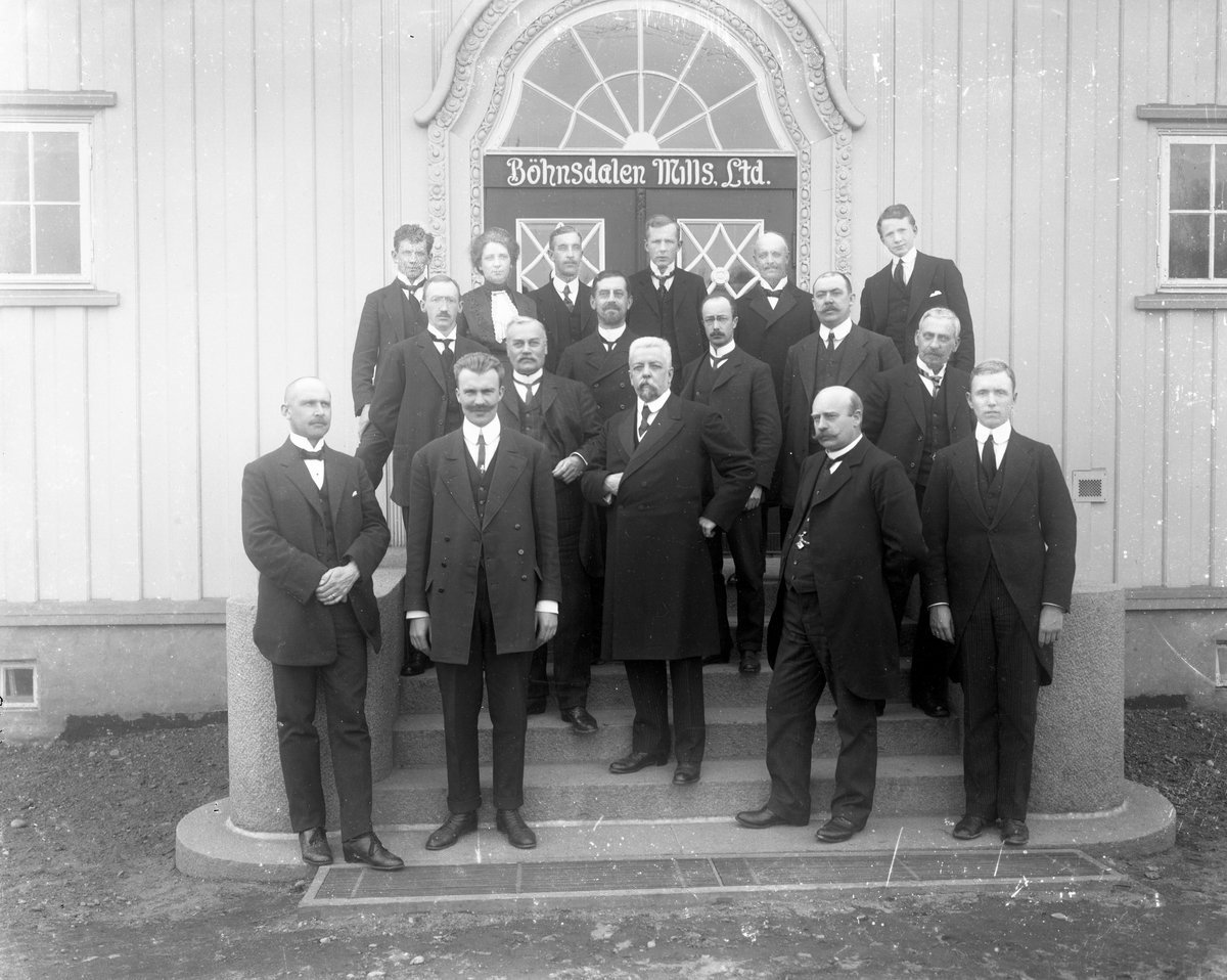 Gruppe menn i dress på trapp foran bygg med Bøhnsdalen Mills Ltd over døra. Bøn, Eidsvoll, Akershus. Nummer tre fra venstre, bakre rekke, er Olaf Gunderson f. 30.10.1881, på Hillringsbeg, Glava, Sverige. Han var ansatt som verksmester, ingeniør på Bøhnsdalen Mills fra 1910 til 1920. Var en av grunnleggerne av firmaet Alfsen & Gunderson.