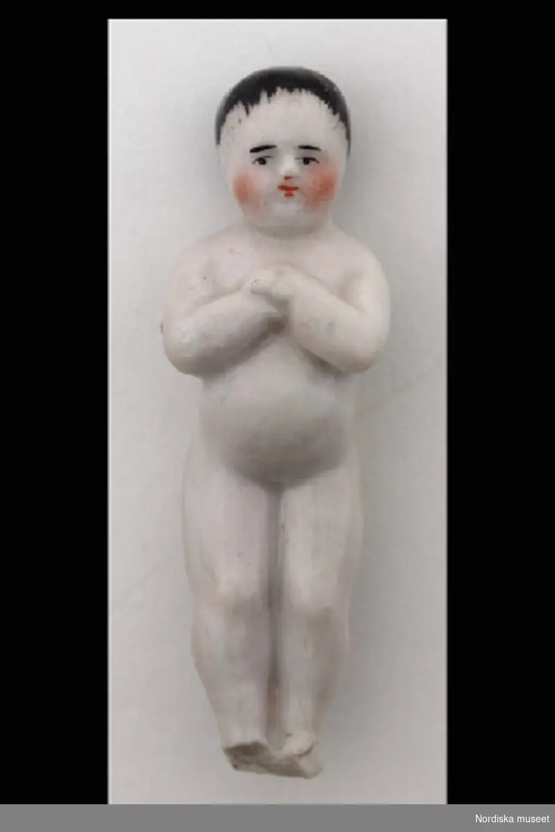 Inventering Sesam 1996-1999:
L  5,5  cm 
Docka, "Frozen Charlie" eller möjligen grötdocka, av porslin, naket gossebarn.
Fötterna avslagna.
Birgitta Martinius 1996