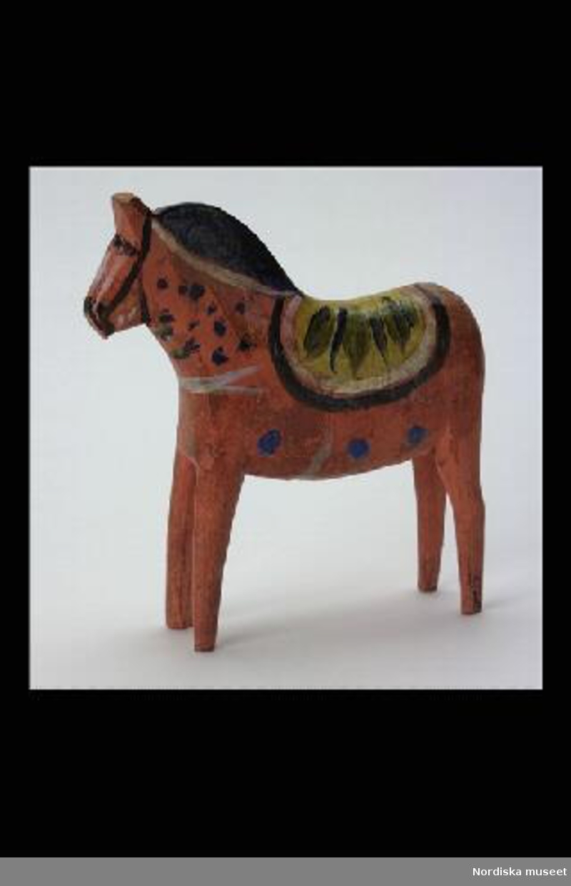 Inventering Sesam 1996-1999:
L 16,5 H 17,5 B 4 (cm)
Häst av trä, rödmålad med krusning i gult, blått, svart och vitt. 
Delvis bestruken med gulnad fernissa. 
Birgitta Martinius 1996