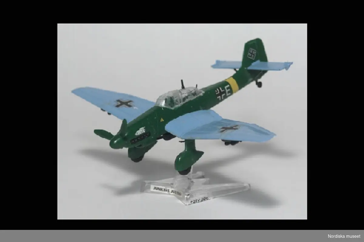 Inventering Sesam 1996-1999:
H ca 4,5 cm
L 14 cm
B 19,7 cm
Modell av tyskt bombplan, Junkers IU 87 Stuka. Grön kropp, Ljusblå vingar. Stjärten dekorerad med hakkors. Lös propeller (ett blad avbrutet). Ställning av ofärgad plast, H 6 cm. med etikett: "JUNKERS JU 87 STUKA". Gjuten märkning: "MATCHBOX".
Placerad på översta hyllan i Mikaels bokhylla, östra väggen.
Ingår i barnrumsinredning inköpt i samband med 1979 års hemundersökning (SAMDOK). Rummet delas av Stefan, f. 1968 och Mikael, f. 1971. Fadern major och modern dagbarnvårdare. Familjen bosatt i radhus i Åkersberga, Vaxholms kommun. Se artiklar i Meddelanden från KU nr 103/1979, SAMDOK-bulletinen nr 8/1979 och Svenska museer nr 1/1980. Intervjumaterial m.m. i arkivet.
Bilaga; förteckning över förvärvet.
AT 1980 [=Annika Tyrfelt]
