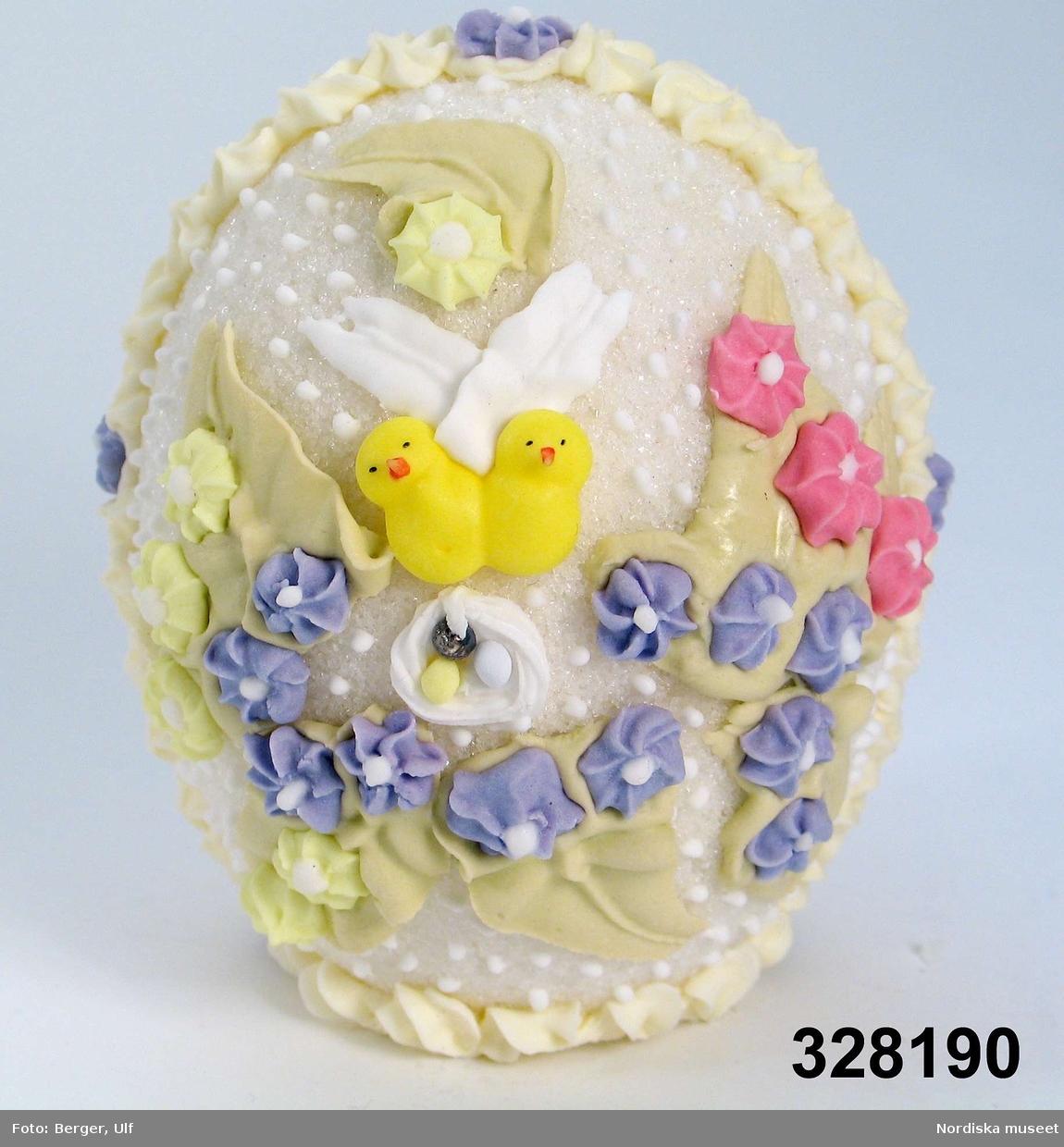 Tittägg i vit kristyr. Utsidan dekorerad med blå, gula och rosa blommor, två kycklingar och rede med ägg samt gröna blad. Genom titthålet  landskap med flicka i rosa klänning av papper (bokmärke) med docka, vit kanin och gul kyckling och rede med ägg samt blommor i blått, rosa och vitt.

Ägget är vid försäljning exponerat i en genomskinlig celluloidask med botten av papp i guldfärg. Ett gult sidenband med rosett är bundet runt asken. Asken ej förvärvad. 
Ägg tillverkade av Kerstin och Peter Hammarström (tillverkade hemma i deras kök) har enl uppgift av Karla frukt, Karlavägen varit ett mycket populärt kristyrägg. 1996 visades tillverkning av kristyrägg på Nordiska museet och kristyrägg såldes i butiken. 
/2005-03-08 Elisabeth Brundin