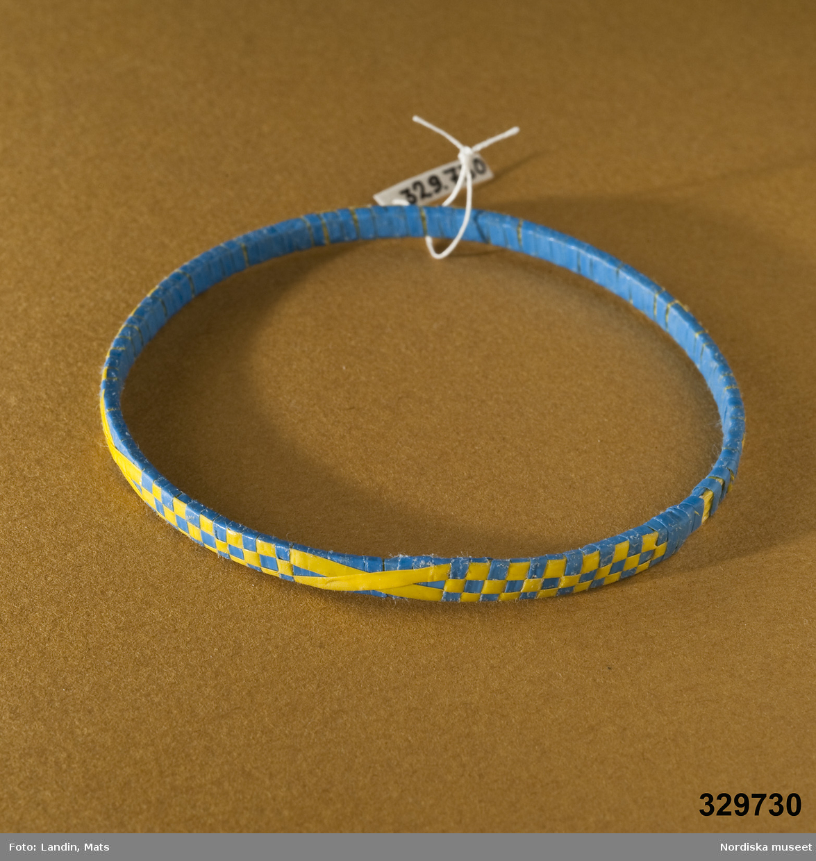 Runt armband med mönster vävt av tunna plastband. Mönster i form av gula/blå rutor och kors. Afrikanska influenser.
Inv.nr 329.728-329.730 är likadana.
/Zingoalla Rosenqvist 2009-02-05