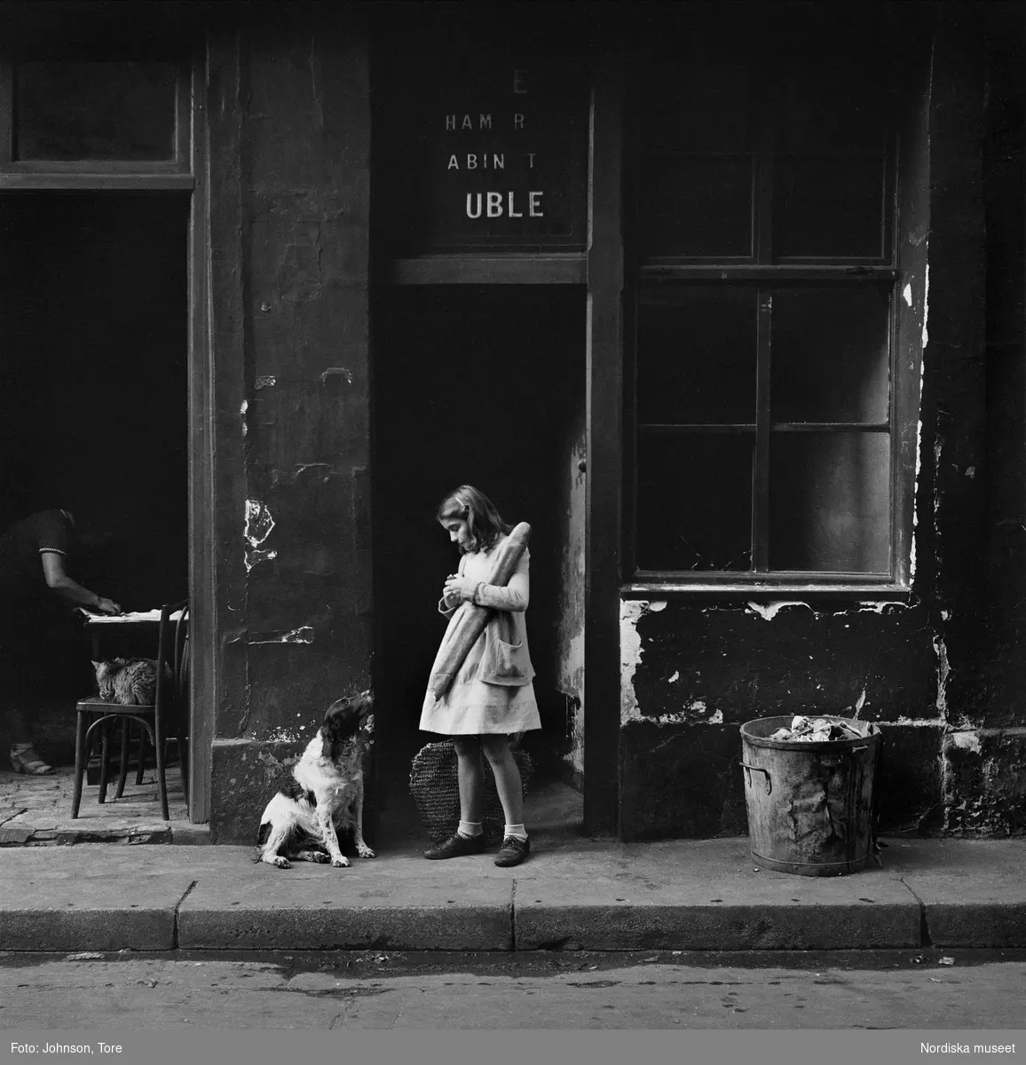 Flicka och hund på trottoar i Paris. Flickan håller i ett långt bröd.