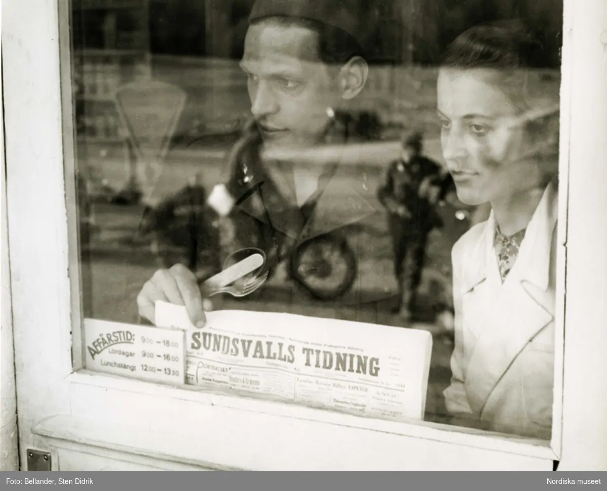 Repmånad. En soldat och en ung kvinna ser ut genom glasdörren till en affär. I glaset reflekteras två andra soldater varav en på motorcykel.
Sundsvalls tidning.