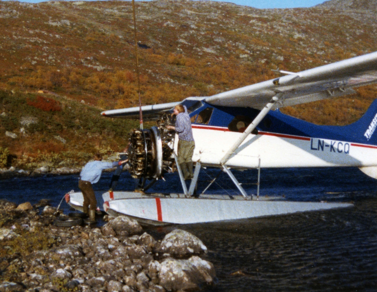 Ett fly i vannkanten, LN-KCQ, DHC-2 Beaver. Flymotoren henger i ei stropp fra Helikopter. To personer ved flyet