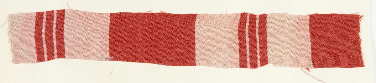 Vävprov ämnat för bolstervarstyg, satinbindning. Randigt i rött och vitt. Vävprovet är uppklistrat på en kartong i storleken 22 x 28 cm. I övre högra hörnet finns en stämpel "Uppsala läns hemslöjdsförening" och ett handskrivet nummer, "A.1585".