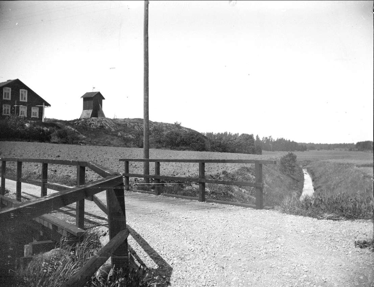Bro över dike, Lovö socken, Uppland 1914. I bakgrunden Lovö kyrkas klockstapel