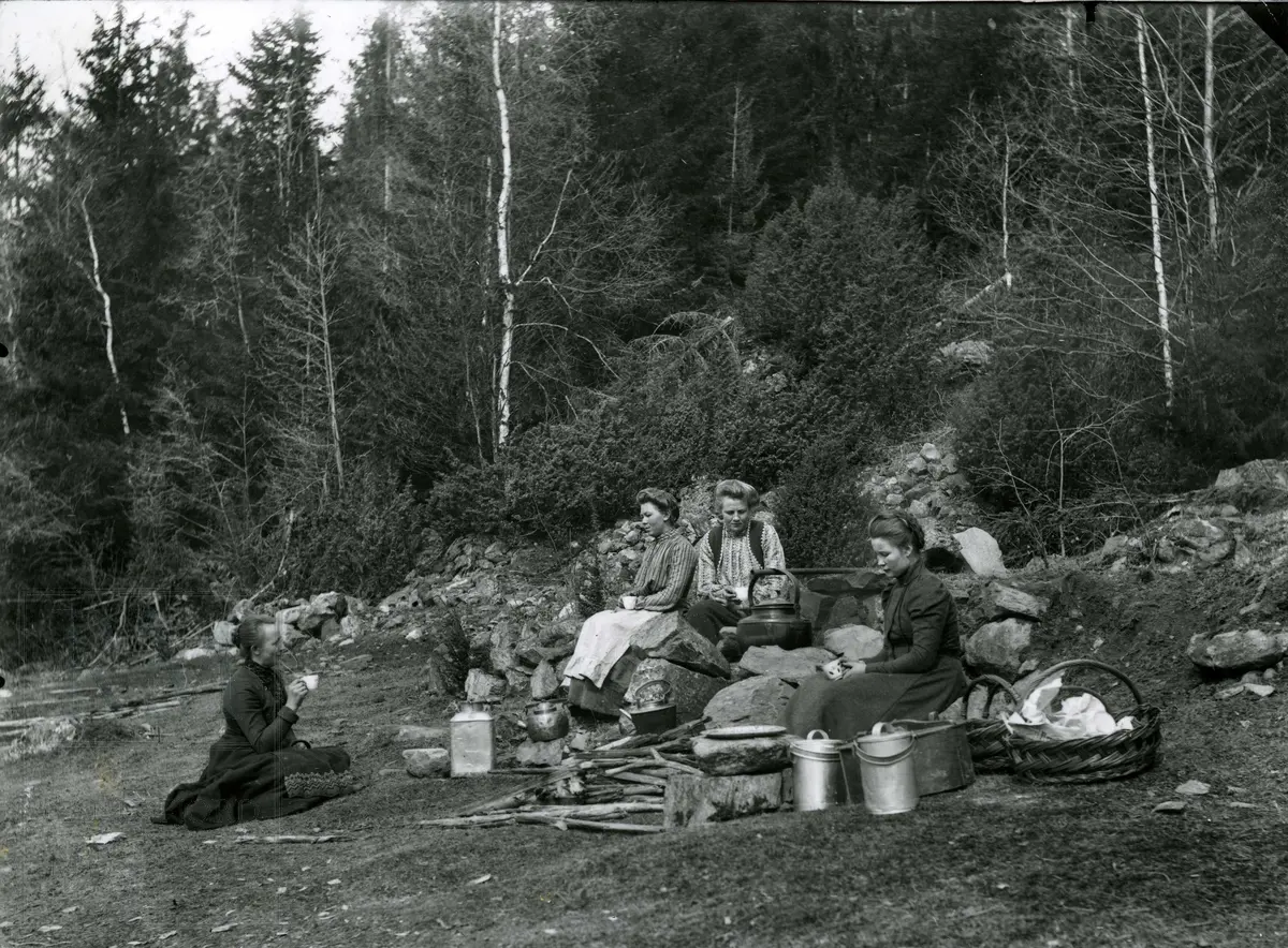 Fire damer med kurver, spann og kaffekjeler sitter rundt ildsted. Matpause under skogplanting ved Lykjalykja.