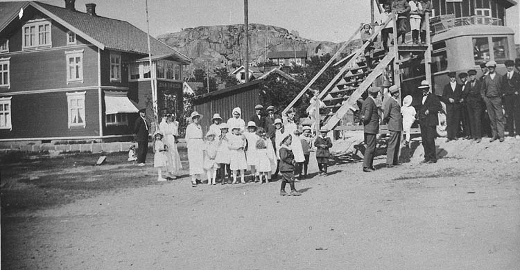 Enl. tidigare noteringar: "Busstationen i Bovallstrand. Bland folket på bilden flera finklädda barn. Ställning med trappa för lastning på busstak. 
Repro 1985 av foto tillhörande Gustav Rundberg, Bovallstrand".