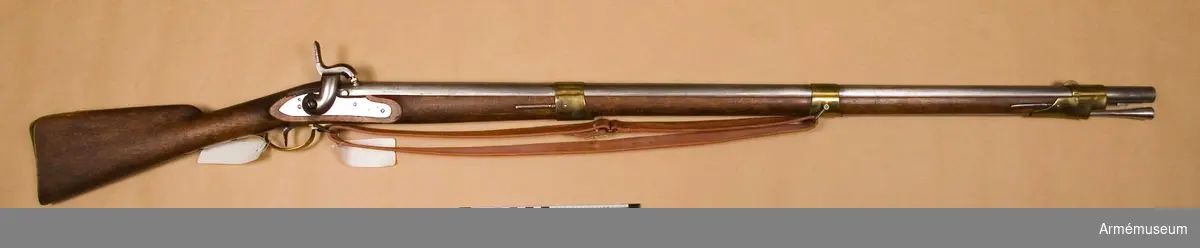 Grupp E II B.
Reparationsmodell.
Geväret är ursprungligen ett i Carl Gustafs stads gevärsfaktori tillverkad flintlåsgevär m/1815-38, se AM 24100, vilket år 1855 ändrats vid Stockholms gevärsförråd till slaglåsgevär enligt 1849 års modell, se AM 1932:4404. Geväret överensstämmer helt med AM 4404. På pipans översida står krönt S (Stockholms gevärsförråd), OC och PIF. På under- sidan är inslaget P, 2, 1855 och 943. På svansskruvsstjärtens undersida står 489. På låsbleckets utsida står 489 och ett krönt C, på insidan GE. Bakom varbygelns baksida är på kolven inslaget AW och på stock- ens V sida bakom sidblecket står 489. På bakplåten är inslaget ett senare med inhuggna punkter kasse- rat tresiffrigt nummer och dessutom numret 489. På varbygelns bakre arm finnes ett monogram av AL, på sidblec- kets insida står B och på insidan av näsbandet och nedre bandet en stämpel med IG. På laddstockens stötyta är bokstaven M inslagen.