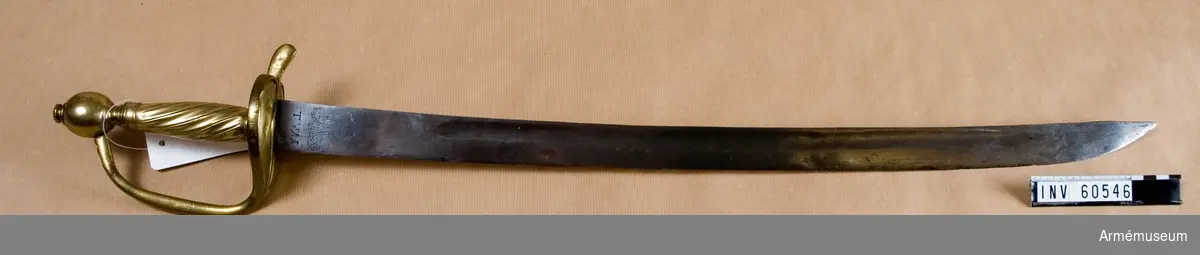 Grupp D II.
Huggare, tillverkad 1770 i Tula, Ryssland.
Klingan prydds av Katarina II:s namnchiffer.
På parerplåtens vänstra framsida står: .N.2.7. (?). inristat, och på högra framsidan står: 2.4 (?).7.6. inristat, fyran kanske är en kyrillisk bokstav. 
En liten oläslig stämpel finns på handbygelns vänstra sida. 
Kavelns "lindning", som bara finns på halva kaveln, sitter på fel sida för då man bär huggaren syns bara den släta sidan kaveln, kanske har den vridits ett halvt varv vid någon reparation?
