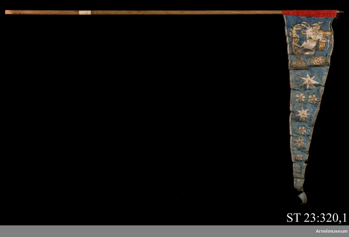 Entungad lansfana. Duk av blå kinesisk sidendamast med målad dekor. I 1703 års inventarium anges motivet vara St Göran men enligt den ryska inskriptionen är det Feodor Stratilat . Rosor och stjärnor av silver. Duken kantad med en silverbård. Strumpa av rött linne.