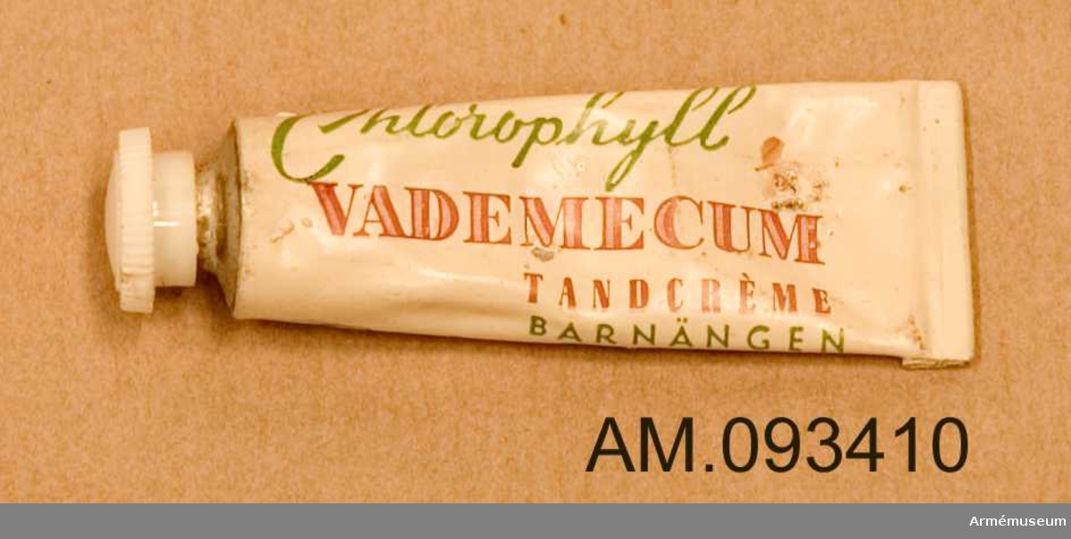 Liten vit tandkrämstub av märket Vademecum med skruvkork och grön och röd text. Innehåller tandkräm.