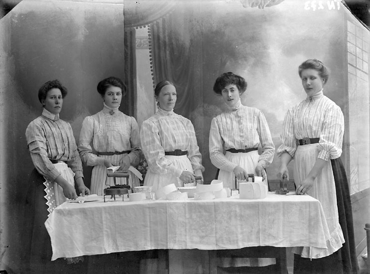 Enligt senare noteringar: "Ateljéfoto, gruppbild av kvinnliga pressare vid bord med strykjärn och kragar och manschetter."