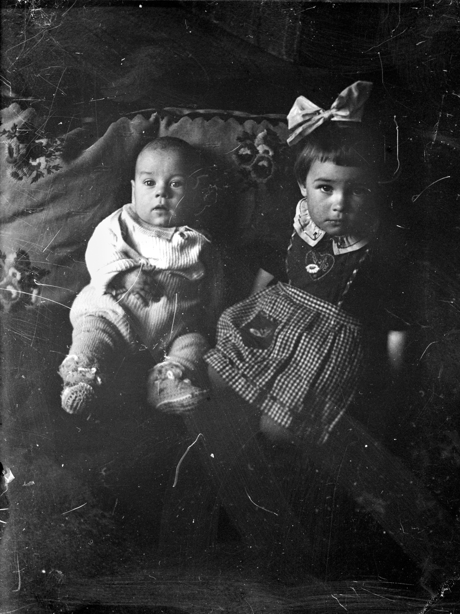 Ett spädbarn och en liten flicka sitter lutade mot en kudde.