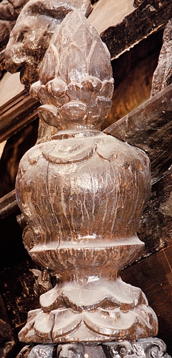 Rundskulpterad och profilerad kupolknopp.
Kupolknoppens mittparti kan liknas vid ett klot. Från dess mitt är klotet insvängt, för att nedtill åter svänga ut något .Ytan är slät, så när som på en "krage" av enkel bladdekor, skurna i låg relief på klotets övre del.

Kupolknoppen avslutas upptill av ett mindre ornament, åtskilt från mittpartiet av en vulst. Ornamentet är snidat som en hårt sluten blomsterknopp, med dubbla lager av foderblad.

Kupolknoppens nedre del består av en kraftig åtta-kantig tapp. Tappen är avskild från det klotformade mittpartiet genom en kragliknande vulst, bestående av enkel bladdekor.

Ett större parti av den upptill avslutande blomsterknoppen, liksom ett stycke av mittpartiets ovansida, är borthugget och bildar ett urtag.

Skulpturen är mycket välbevarad.

Text in English: Sculpted and ornamented three dimensional knob.
The knob''s middle section is shaped as a globe. From its middle part it curves inwards and lower down curves outwards again. The globe is smooth except for a "collar" of simple leaf decoration, carved in shallow relief on the globe''s upper part.

On top of the globe sits a smaller ornament. This is separated from the globe by a tenon. The ornament is shaped like a smaller flower bud and has a double layer of sepal.

The knob has a heavy, eight-sided tenon at the bottom. It is separated from the globe by a collar-like torus. The torus has a simple leaf decoration.

A large section of the top flower bud and a section of the middle has been cut away forming an indentation.
The sculpture is very well preserved.
