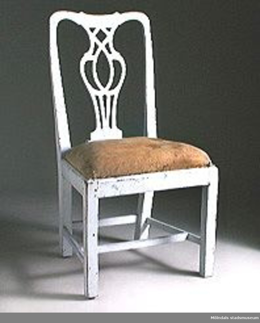 Stol, genombruten ryggbricka, raka ben med kvadratisk genomskärning. H-kryss samt slå mellan de bakre benen.Tillverkad i Lindome 1760-80-tal.Stolens ryggbricka återgår på en förlaga av den engelske möbelformgivaren Thomas Chippendale (verksam vid mitten av 1700-talet). Stolen har framtagen rödbrun originalfärg (vid förvärvet var stolen målad i en sentida gråvit lackfärg).Lös sits med originalsadelgjord och stoppning. Inköpta av Per Falck, intendent vid Nordiska museet, för Mölndals museums räkning av antikhandlare Bengt Jansson i Älmhult.En stol stulen 2002.