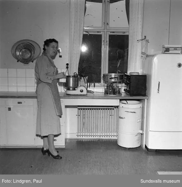 Fru Lindlöf i sitt kök, samt två pojkar som hjälper till med disken.