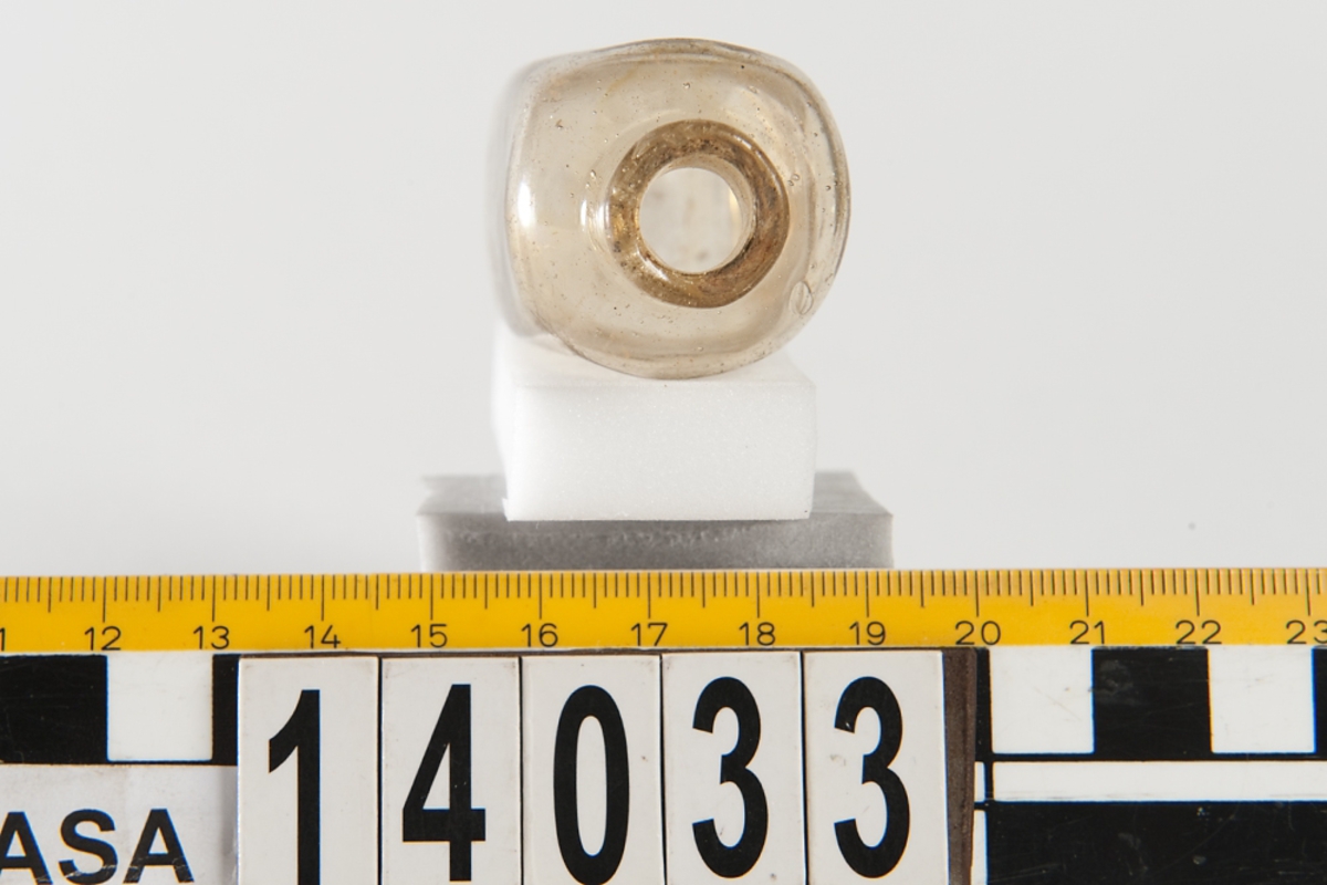 En gul-brun fyrsidig glasflaska.

Small glass medicine bottle. No damage to the artifact but the bottle has a misshapen shoulder from the manufacturing process. Glass is clear with a brownish tint, possibly potash-lime glass.