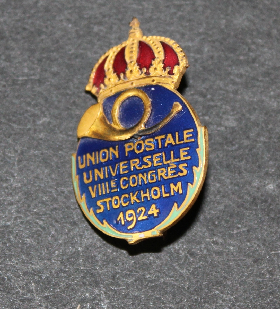 Deltagarmärke för delegaterna vid VIII Världspostkongressen i
Stockholm 1924.Posthorn i guld på blå guldkransad emaljerad sköld.
Däröver krona i guld och rött.