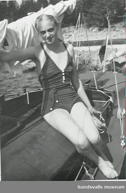 Kvinna i baddräkt sitter på en segelbåt.