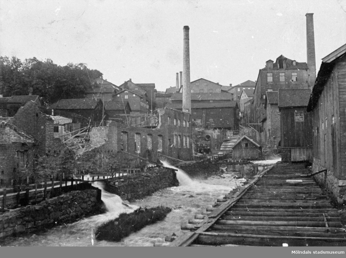 Nedre delen av forsen (Mölndalsfallen) uppströms Forsebron, sommaren 1894. Till höger ses kvarnrännan.
I förgrunden till vänster ses ruinerna efter Delbancos fabrik som brann sommaren 1894.