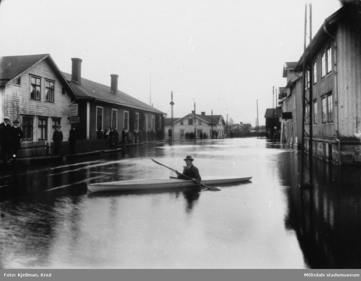 Översvämning vid Mölndalsbro, 1930-tal. Gösta Viktorinus paddlar omkring i kanot. Från vänster ses skomakare Gustaf Adolf Petterssons fastighet, spårvagnshallarna, bankhuset (Kungsbackavägen 1), Stibergs (Kungsbackavägen 2) samt Göteborgsvägen 1, 3 och 5.