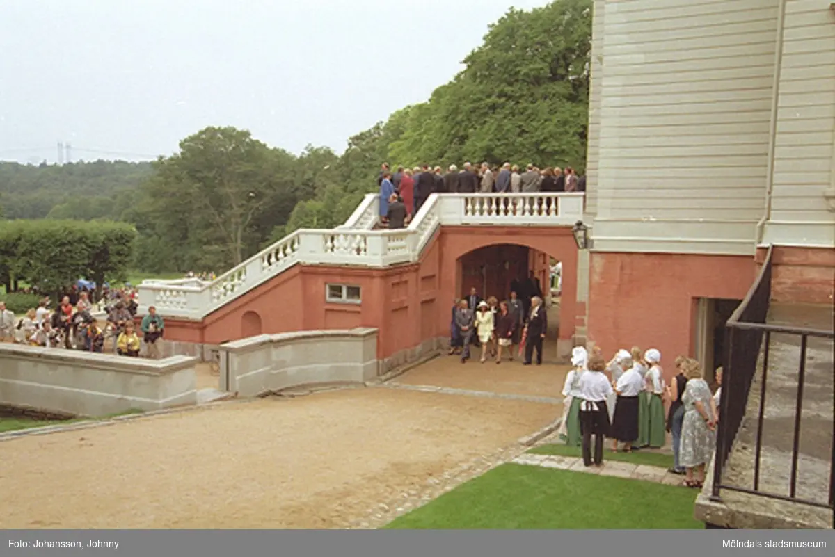 Besökare till vänster och kommunanställda på terrassen tittar på när kungaparet är på besök och promenerar under Gunnebo slottsterrass, 1997-08-27. Till höger ses slottets egen personal.