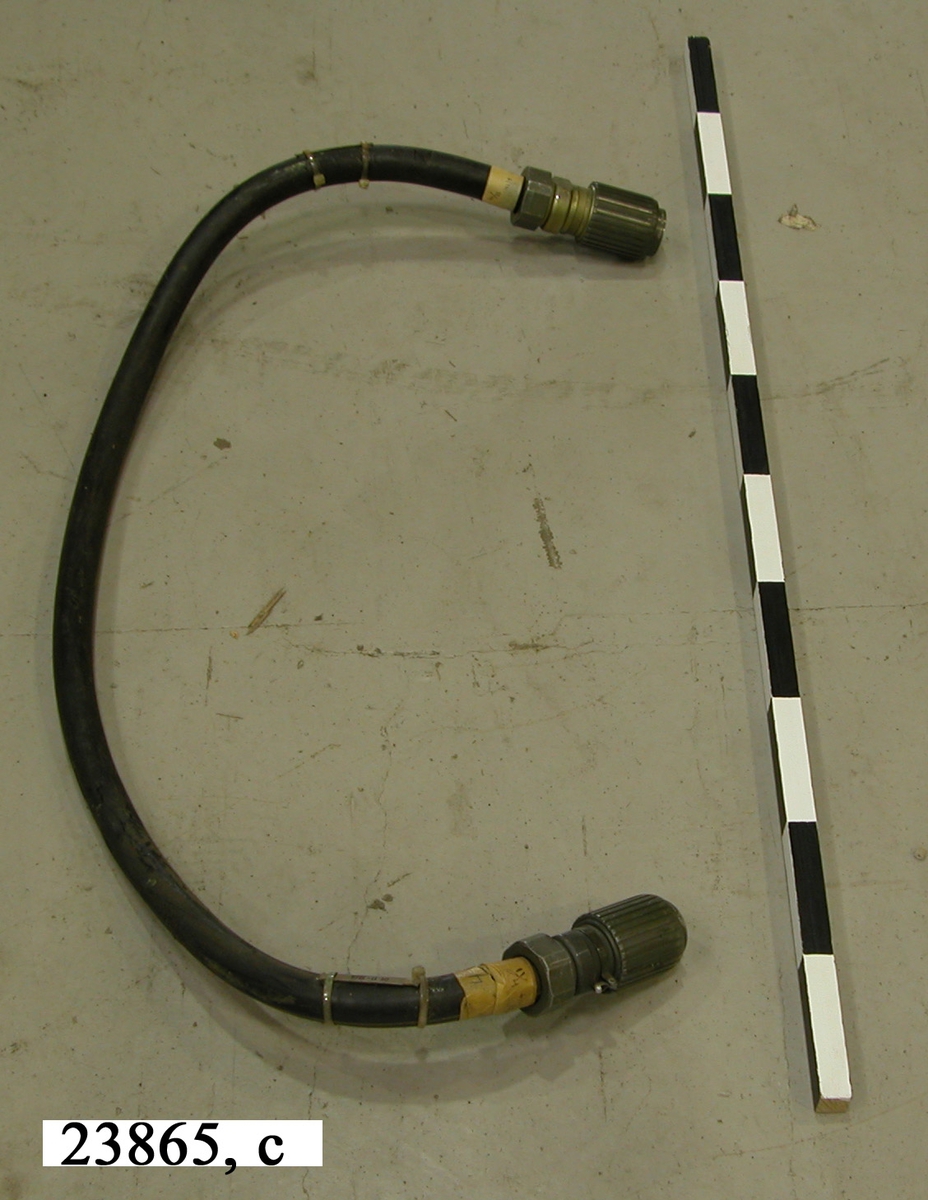 Kabel av gummi. I ändarna sitter grönlackerade kopplingsanordningar av aluminium. Kopplingarna har ytterst gängade hylsor vilka används för att låsa bakeln till instrumentet.