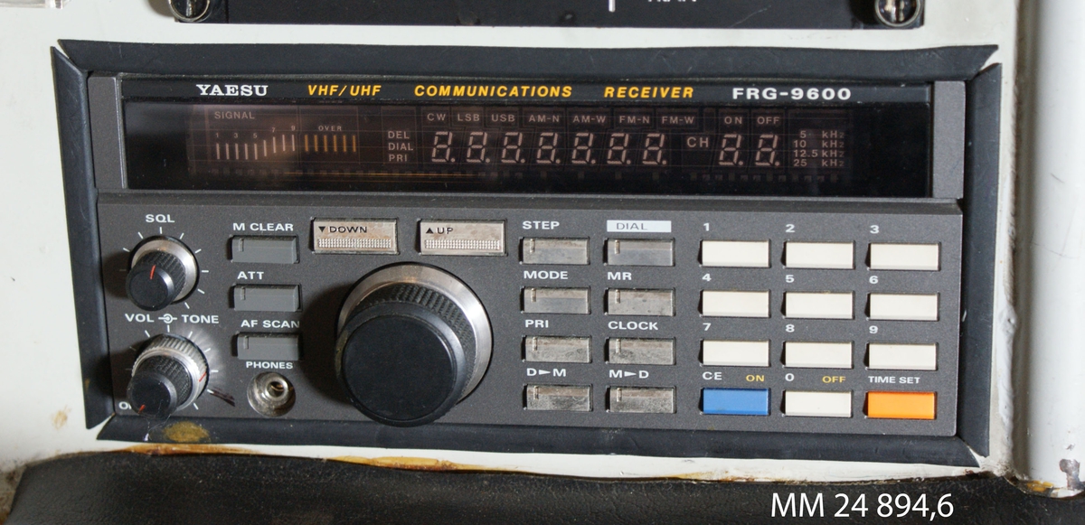 Radiomottagare YAESU (FRG 9600). Rektangulär grå apparat med tre rattar och diverse knappar i grått, vitt, blått och orange. Rektangulär digital display längs med apparaten. Kapacitet 99 kanaler, 60-905 MHz.