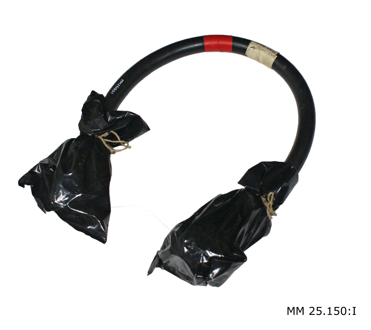 Svart gummiklädd kabel med metallkopplingsdon i ändarna. Mitt på sitter papperstejpbit lind med tuschtext: "F1105-208191 Kopplingskabel 3628-001". Kopplingskontakterna är inklädda i plastpåsar av svart plast som är förslutna med rep.