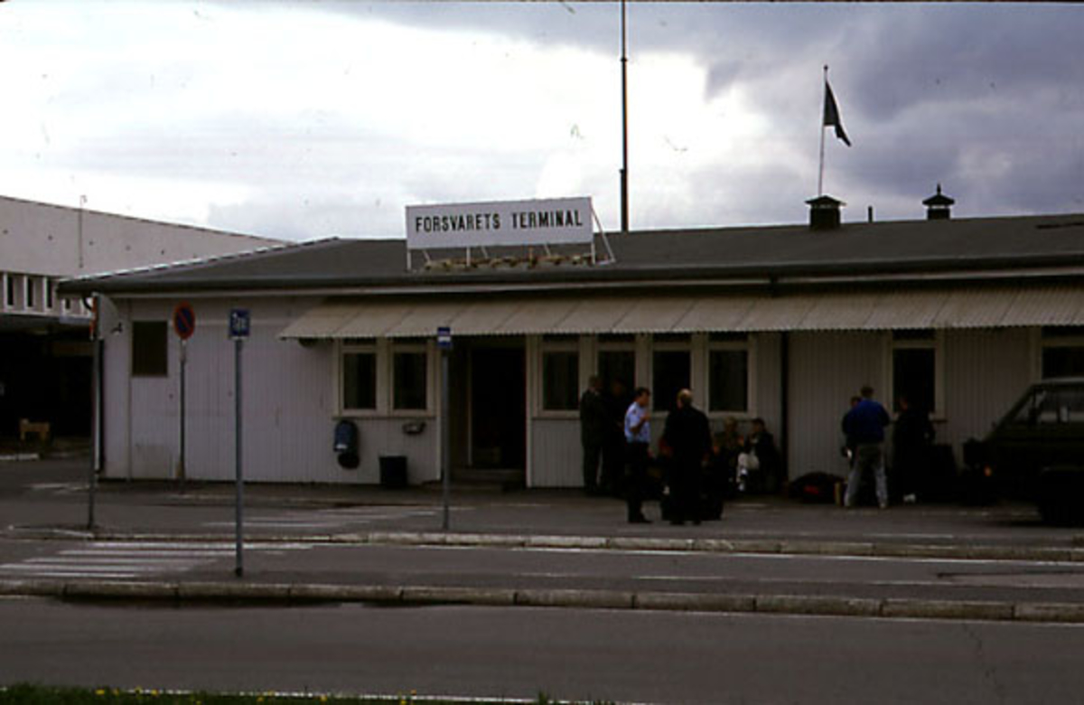 Lufthavn, flere personer foran bygning. Bygningen med påskrift "Forsvarets Terminal".