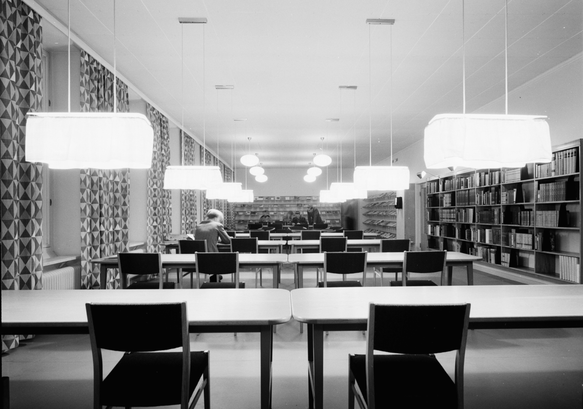 Stadsbibliotek i Umeå
Interiör. Läsesal, rader av bänkar och stolar efter varandra, med lysande lampor från taket.
