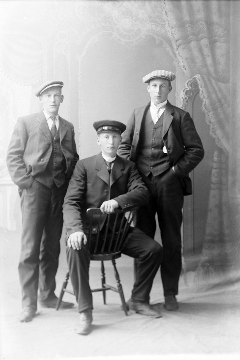 Studioportrett av tre unge menn i helfigur. Mannen som sitter i midten er Fredrik Fredriksen på Kilhus.