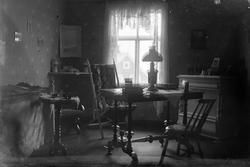 Interiørbilde av et rom med bord, stoler, lampe, kommode og 