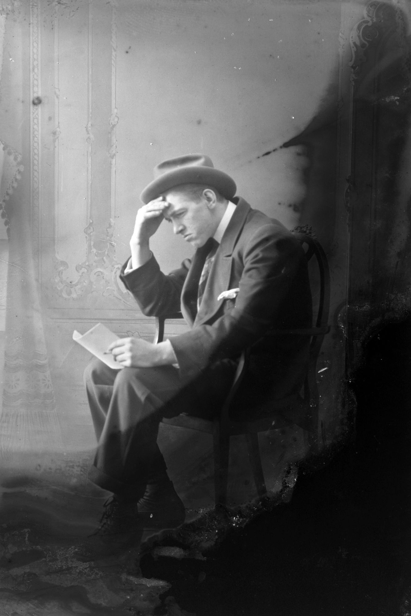 Studioportrett av en sittende mann som støtter hodet med høyre hånd mens han leser en bok.