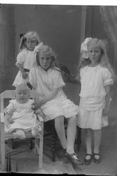 Studioportrett av tre unge piker og en baby i lyse klær.