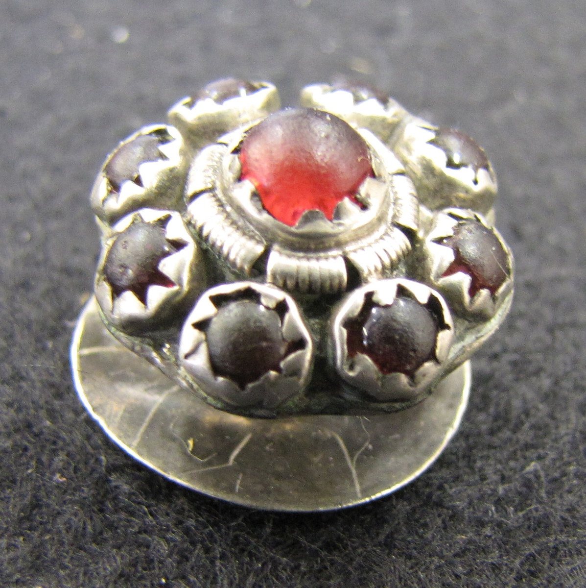 Allmogeknapp av silver, manschettknappsmodell, med nio infattade röda glaspärlor.