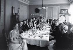 Bryllupsfest. Brudepar og gjester ved bordet i stua. Bstille