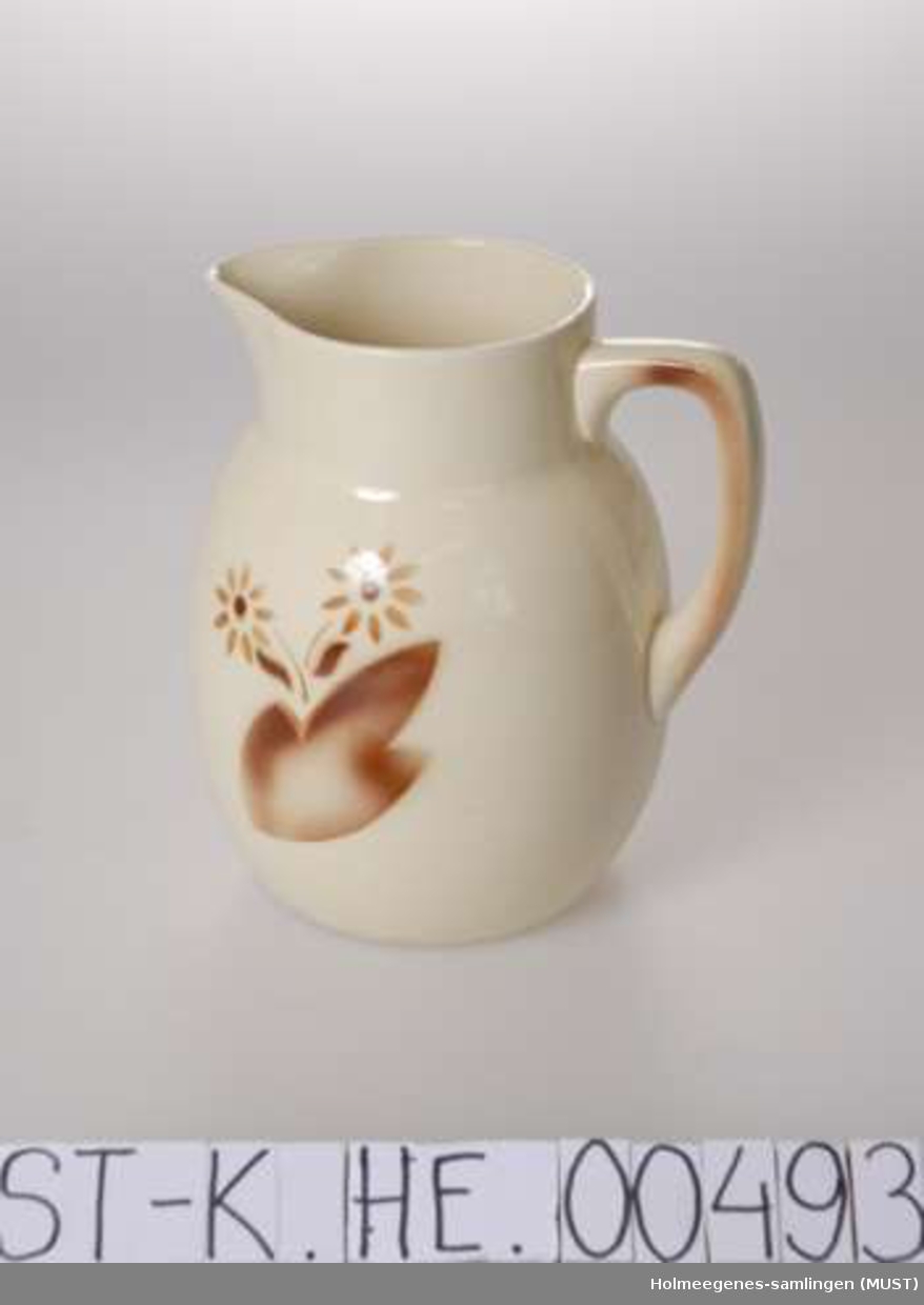 Vannsmugge av keramikk. Gulhvit glasur med brun dekor i form av abstraherte blomster på korpus, og et enkelt strøk på hanken.