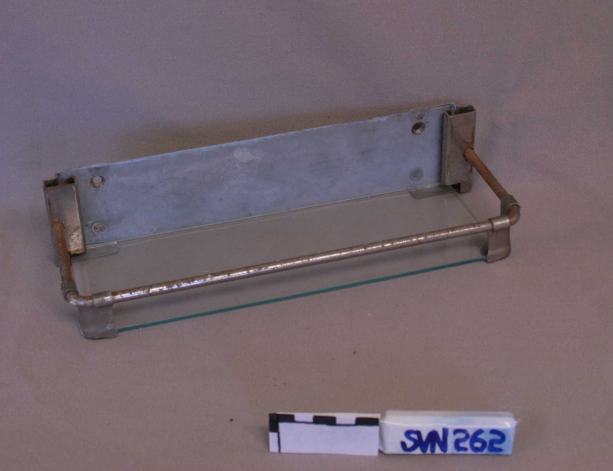 Hylle i to deler:
Del A: Metallramme monter på rektangulært veggheng. 
Del B: Hylleplate i gjennomsiktig glass